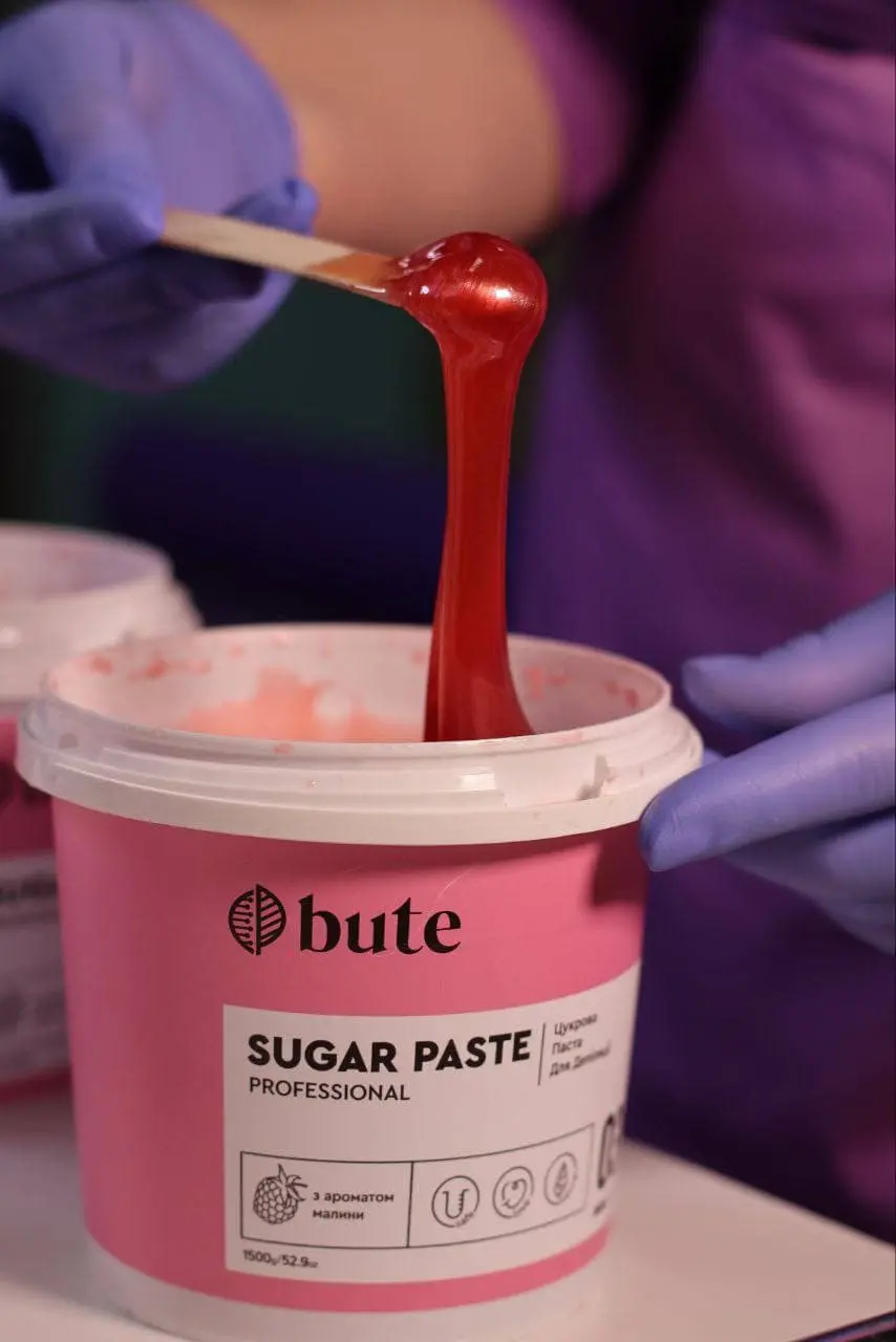 Цукрова паста на шпателі над пластиковою банкою.